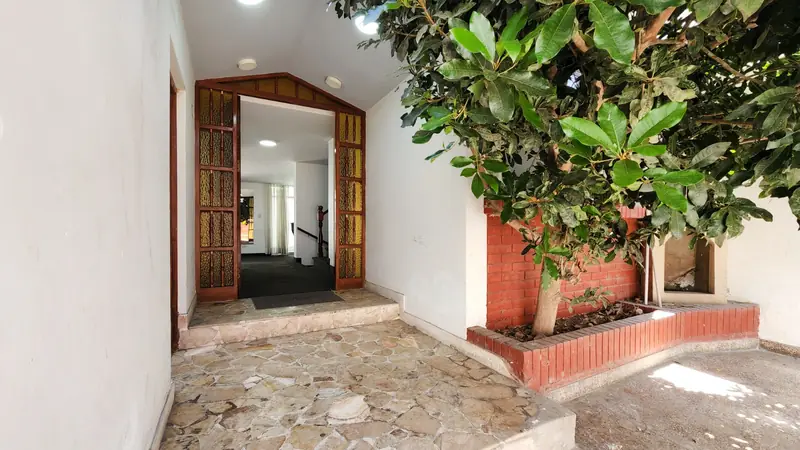 Ingreso de la casa en San Miguel con piso de piedra, jardinera de ladrillo y puerta de madera